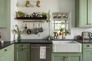 Inspiration for a mid-sized eclectic l-shaped separate kitchen in Philadelphia with a farmhouse sink, shaker cabinets, green cabinets, quartz benchtops, white splashback, ceramic splashback, stainless steel appliances, porcelain floors, no island, beige floor and black benchtop.