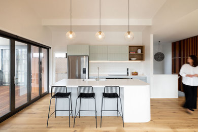 Large contemporary galley open plan kitchen in Auckland with a double-bowl sink, composite countertops, white splashback, ceramic splashback, stainless steel appliances, medium hardwood flooring, an island and white worktops.
