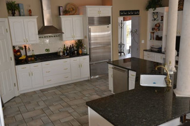 Large transitional l-shaped eat-in kitchen in Detroit with a drop-in sink, raised-panel cabinets, yellow cabinets, laminate benchtops, white splashback, cement tile splashback, stainless steel appliances, porcelain floors and multiple islands.