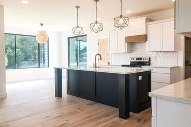 Inspiration for a mid-sized farmhouse l-shaped light wood floor eat-in kitchen remodel with an undermount sink, shaker cabinets, white cabinets, quartz countertops, white backsplash, ceramic backsplash, stainless steel appliances, an island and white countertops