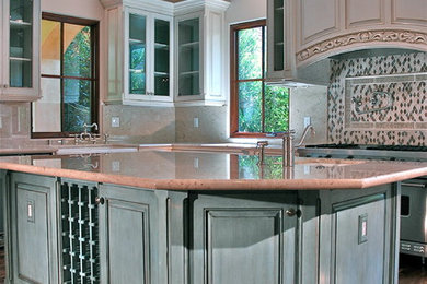 Example of a mid-sized tuscan u-shaped medium tone wood floor eat-in kitchen design in Los Angeles with a farmhouse sink, glass-front cabinets, beige cabinets, marble countertops, beige backsplash, stone slab backsplash, stainless steel appliances and an island