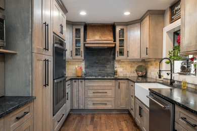 Photo of a mid-sized country eat-in kitchen in Raleigh with a farmhouse sink, shaker cabinets, light wood cabinets, soapstone benchtops, multi-coloured splashback, travertine splashback, stainless steel appliances, dark hardwood floors, a peninsula, multi-coloured floor and black benchtop.