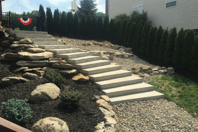 Photo of a mid-sized rustic drought-tolerant and full sun hillside river rock and metal fence retaining wall landscape in Cleveland.