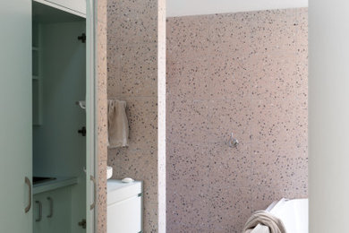 This is an example of a mid-sized eclectic master bathroom in Melbourne with flat-panel cabinets, green cabinets, a drop-in tub, an open shower, a two-piece toilet, pink tile, stone tile, pink walls, terrazzo floors, a vessel sink, laminate benchtops, pink floor, an open shower, green benchtops, a laundry, a single vanity and a built-in vanity.