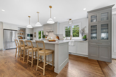 Large transitional l-shaped medium tone wood floor and brown floor eat-in kitchen photo in Ottawa with a farmhouse sink, shaker cabinets, gray cabinets, quartz countertops, white backsplash, quartz backsplash, stainless steel appliances, an island and white countertops