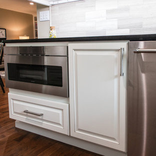 Inspiration pour une grande arrière-cuisine parallèle traditionnelle avec un évier encastré, un placard avec porte à panneau surélevé, des portes de placard blanches, un plan de travail en quartz, une crédence multicolore, une crédence en pierre calcaire, un électroménager en acier inoxydable, un sol en bois brun, un îlot central et un sol marron.