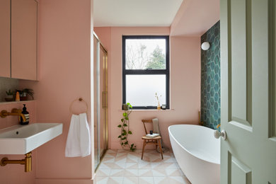 Photo of a medium sized contemporary family bathroom in London with a freestanding bath, a built-in shower, a wall mounted toilet, pink tiles, ceramic tiles, pink walls, cement flooring, a wall-mounted sink, terrazzo worktops, pink floors, a sliding door, multi-coloured worktops, a feature wall, a single sink and a built in vanity unit.