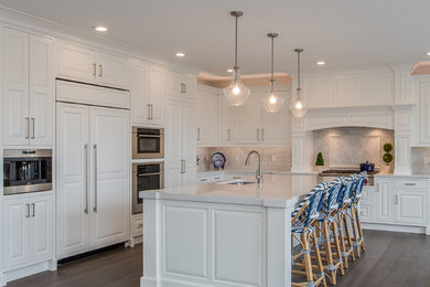 Design ideas for a large transitional l-shaped open plan kitchen in Boston with an undermount sink, raised-panel cabinets, white cabinets, quartz benchtops, white splashback, subway tile splashback, stainless steel appliances, medium hardwood floors, with island, brown floor and white benchtop.