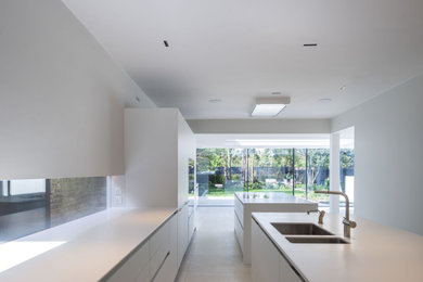 Expansive modern open plan kitchen in London with a double-bowl sink, flat-panel cabinets, grey cabinets, composite countertops, white splashback, limestone flooring, multiple islands, beige floors, white worktops and feature lighting.