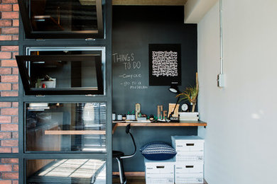 Industrial home office in Other with white walls, medium hardwood floors, a built-in desk and brown floor.