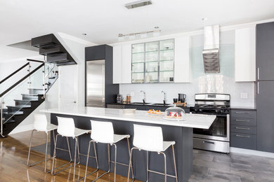 Example of a trendy gray floor open concept kitchen design in New York with an island, a double-bowl sink, stainless steel cabinets, white backsplash, subway tile backsplash, stainless steel appliances, black countertops and flat-panel cabinets