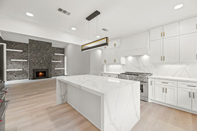 This is an example of a modern kitchen in Houston with shaker cabinets, white cabinets, engineered stone countertops, multi-coloured splashback, stone slab splashback, light hardwood flooring and an island.