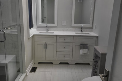Example of a trendy porcelain tile porcelain tile, white floor and double-sink double shower design in Toronto with a built-in vanity, shaker cabinets, white cabinets, a one-piece toilet, gray walls, an undermount sink, quartz countertops, a hinged shower door and white countertops