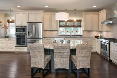 Kitchen - large country l-shaped dark wood floor kitchen idea in Kansas City with recessed-panel cabinets, beige cabinets, granite countertops, beige backsplash, stainless steel appliances and an island
