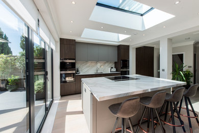 This is an example of a medium sized modern grey and brown open plan kitchen in Other with a single-bowl sink, flat-panel cabinets, grey cabinets, quartz worktops, white splashback, stone slab splashback, black appliances, laminate floors, an island, beige floors, white worktops and feature lighting.