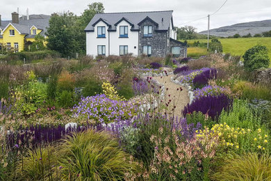 Immagine di un grande giardino country esposto in pieno sole davanti casa in estate con sassi di fiume e recinzione in pietra