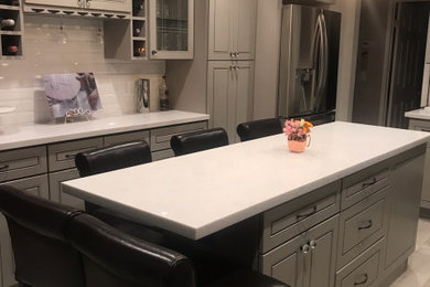 Bild på ett litet vintage flerfärgad flerfärgat kök, med en rustik diskho, luckor med profilerade fronter, grå skåp, bänkskiva i kvarts, vitt stänkskydd, stänkskydd i porslinskakel, rostfria vitvaror, vinylgolv, en köksö och brunt golv