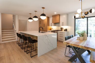 Mid-sized trendy galley laminate floor and brown floor eat-in kitchen photo in Minneapolis with a single-bowl sink, flat-panel cabinets, white cabinets, quartz countertops, white backsplash, porcelain backsplash, stainless steel appliances, an island and white countertops