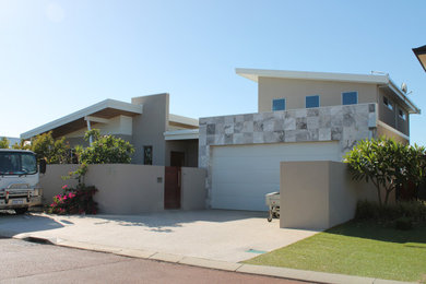 Mid-sized two-storey yellow house exterior in Perth with stone veneer, a butterfly roof and a metal roof.