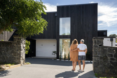 Inspiration for a mid-sized contemporary two-storey brick black house exterior in Auckland with a flat roof, a metal roof and a black roof.