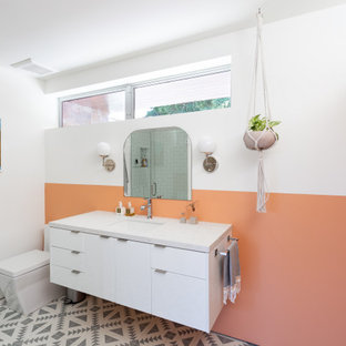 Example of a trendy multicolored floor bathroom design in San Francisco with flat-panel cabinets, white cabinets, orange walls, an undermount sink and white countertops