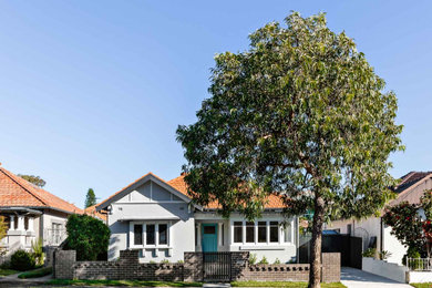 Photo of a mid-sized traditional one-storey stucco grey house exterior in Sydney with a hip roof, a tile roof and a red roof.