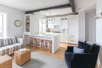 Inspiration for a small beach style single-wall eat-in kitchen in New York with a farmhouse sink, recessed-panel cabinets, white cabinets, quartz benchtops, white splashback, engineered quartz splashback, stainless steel appliances, light hardwood floors, a peninsula and white benchtop.