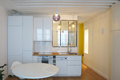 Small contemporary single-wall open plan kitchen in Paris with a single-bowl sink, beaded inset cabinets, white cabinets, wood benchtops, white splashback, porcelain splashback, white appliances, no island and medium hardwood floors.