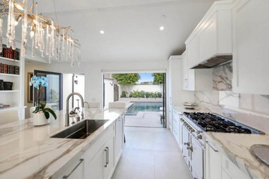 Example of a large beach style galley eat-in kitchen design in Orange County with shaker cabinets, white cabinets, multicolored backsplash and an island