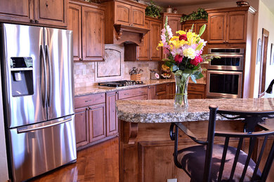 Inspiration for a large rustic galley medium tone wood floor and brown floor eat-in kitchen remodel in Denver with an undermount sink, raised-panel cabinets, medium tone wood cabinets, granite countertops, beige backsplash, stone tile backsplash, stainless steel appliances and an island