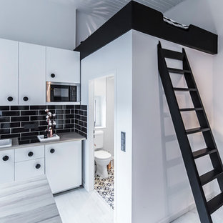 Imagen de cocina comedor lineal, actual, pequeña, con fregadero sobremueble, armarios con paneles lisos, puertas de armario blancas, salpicadero negro, salpicadero de azulejos tipo metro, electrodomésticos de acero inoxidable, suelo de madera clara, encimera de madera y península