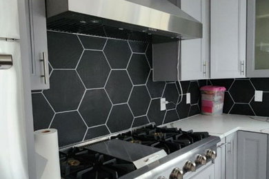 Inspiration for a large modern u-shaped medium tone wood floor and brown floor eat-in kitchen remodel in Philadelphia with a drop-in sink, gray cabinets, quartz countertops, black backsplash, ceramic backsplash, stainless steel appliances, an island and white countertops