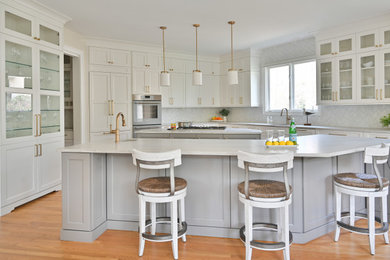 Exempel på ett klassiskt grå grått kök och matrum, med en undermonterad diskho, luckor med infälld panel, vita skåp, grått stänkskydd, integrerade vitvaror, ljust trägolv, flera köksöar och brunt golv