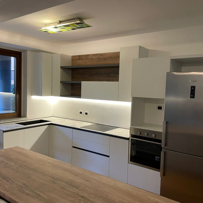 Cucina in finitura Utopia Bianco con maniglia a gola Brunita. Top in HPL color Palladio con lavello un vascone in Keratek Nero sottotop. Per l'isola che divide la cucina dal soggiorno, basi in finitur