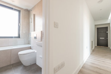 Medium sized modern family bathroom in London with flat-panel cabinets, white cabinets, a built-in bath, a wall mounted toilet, white tiles, porcelain tiles, white walls, porcelain flooring, an integrated sink, grey floors, a single sink and a floating vanity unit.