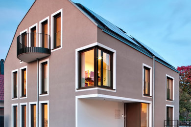 Diseño de fachada beige actual de tamaño medio de tres plantas con revestimiento de estuco y tejado de metal