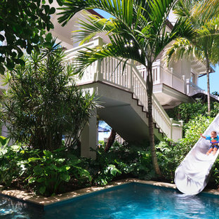 Idée de décoration pour une très grande piscine à débordement et arrière ethnique sur mesure avec un toboggan et des pavés en pierre naturelle.