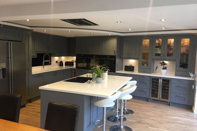 Large classic l-shaped open plan kitchen in Hampshire with a single-bowl sink, shaker cabinets, grey cabinets, composite countertops, white splashback, black appliances, an island and white worktops.