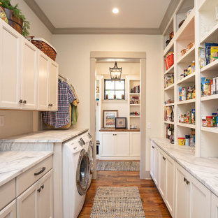 アトランタのカントリー風おしゃれな家事室 (落し込みパネル扉のキャビネット、白いキャビネット、白い壁、無垢フローリング、左右配置の洗濯機・乾燥機、茶色い床、グレーのキッチンカウンター) の写真