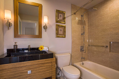 Inspiration for a small tropical 3/4 beige tile and ceramic tile porcelain tile alcove bathtub remodel in Hawaii with a console sink, furniture-like cabinets, medium tone wood cabinets, granite countertops, a two-piece toilet and gray walls