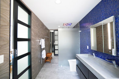 Пример оригинального дизайна: главная ванная комната среднего размера со стиральной машиной в современном стиле с плоскими фасадами, черными фасадами, душем без бортиков, биде, синей плиткой, стеклянной плиткой, серыми стенами, полом из керамогранита, раковиной с несколькими смесителями, столешницей из бетона, серым полом, открытым душем, серой столешницей, тумбой под две раковины и подвесной тумбой