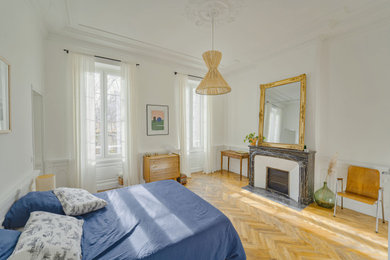 Cette image montre une grande chambre parentale haussmannienne victorienne avec un mur blanc, parquet clair, une cheminée standard, un manteau de cheminée en pierre et un sol beige.