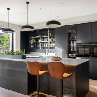 Design ideas for a large contemporary kitchen/diner in Gloucestershire with a built-in sink, flat-panel cabinets, black cabinets, composite countertops, white splashback, black appliances, an island and white worktops.