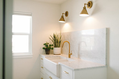 Mid-sized transitional laundry room photo in Other with a farmhouse sink, shaker cabinets, white cabinets, marble countertops, gray backsplash, beige walls, a side-by-side washer/dryer and gray countertops