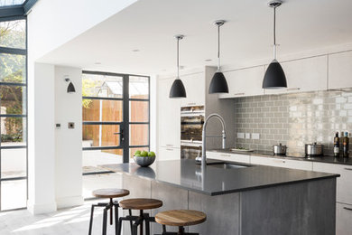 Photo of a mid-sized contemporary galley kitchen in London with an undermount sink, flat-panel cabinets, grey splashback, subway tile splashback, stainless steel appliances, with island, grey floor, grey benchtop, white cabinets and light hardwood floors.