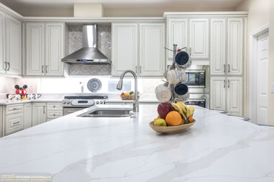 Mid-sized elegant l-shaped porcelain tile and beige floor eat-in kitchen photo in Orlando with an undermount sink, raised-panel cabinets, beige cabinets, quartz countertops, beige backsplash, marble backsplash, stainless steel appliances, an island and white countertops