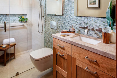 Photo of a small modern bathroom in San Diego with shaker cabinets, medium wood cabinets, a curbless shower, a wall-mount toilet, green tile, glass tile, beige walls, travertine floors, an undermount sink and granite benchtops.