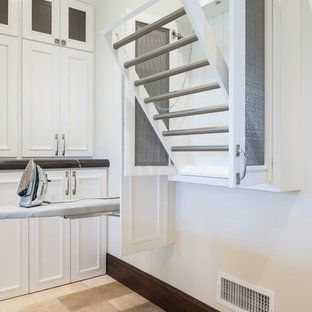 ソルトレイクシティの大きいラスティックスタイルのおしゃれな洗濯室 (落し込みパネル扉のキャビネット、白いキャビネット、ベージュの壁、トラバーチンの床、左右配置の洗濯機・乾燥機、ベージュの床、茶色いキッチンカウンター) の写真