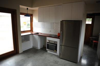 Design ideas for a small country l-shaped eat-in kitchen in Canberra - Queanbeyan with an undermount sink, white cabinets, wood benchtops, white splashback, subway tile splashback, stainless steel appliances and concrete floors.
