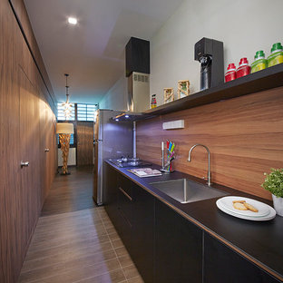 Modern kitchen pantry designs - Inspiration for a modern galley ceramic floor kitchen pantry remodel in Singapore with a drop-in sink, dark wood cabinets, brown backsplash, black appliances and an island
